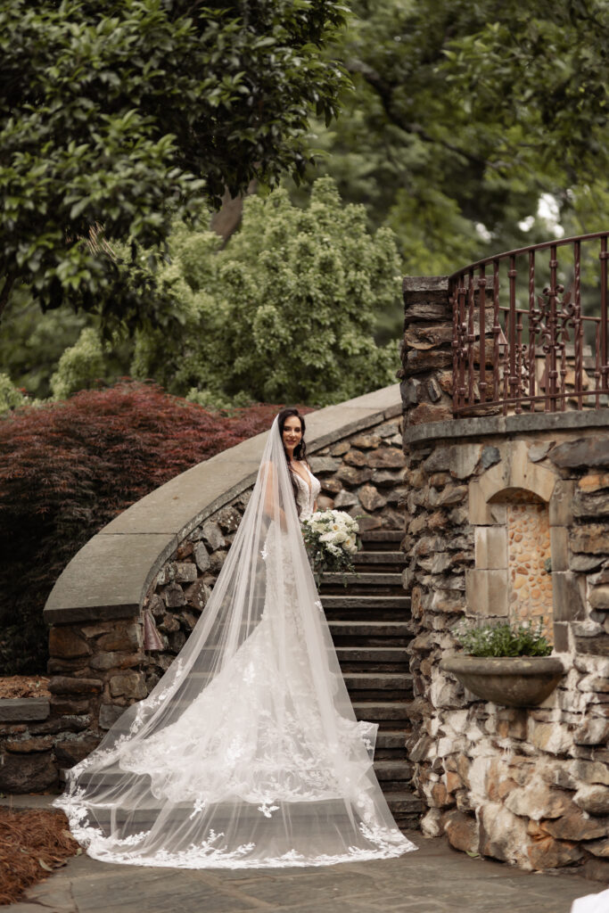 Bride standing on outdoor stone stairs with her veil flowing behind her