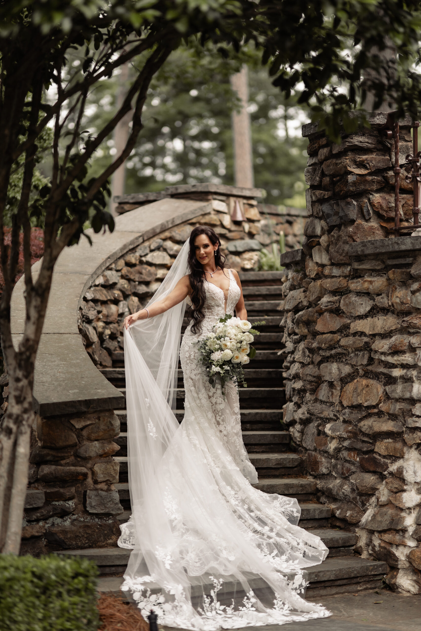 Bride on outdoor stairs holding veil away from her dress while it is draped down the stairs.